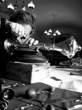 Image of Ray hand engraving the Tasmanian Parliamentary Mace inside Parliament House in Hobart, a selection of gravers, eyeglasses and other tools are in the foreground
