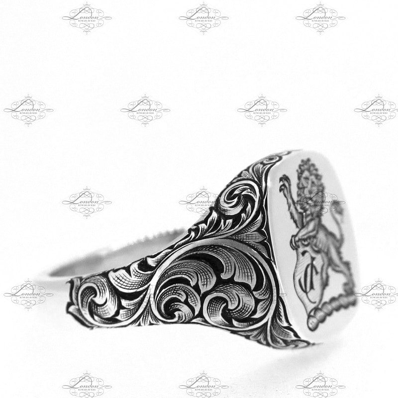 White gold cushion shaped signet ring with scrollwork hand engraved on the shoulders with black enamel added.  Lion Crest surface engraved on the face of the cushion signet ring.