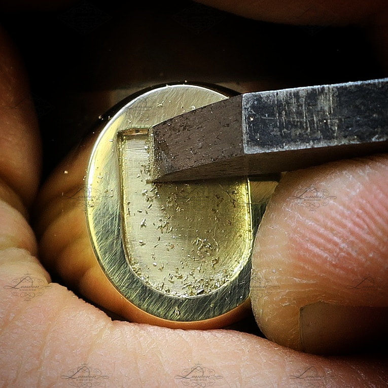 flat scorper graver being used to remove the background of a yellow gold signet ring for a seal engraved shield