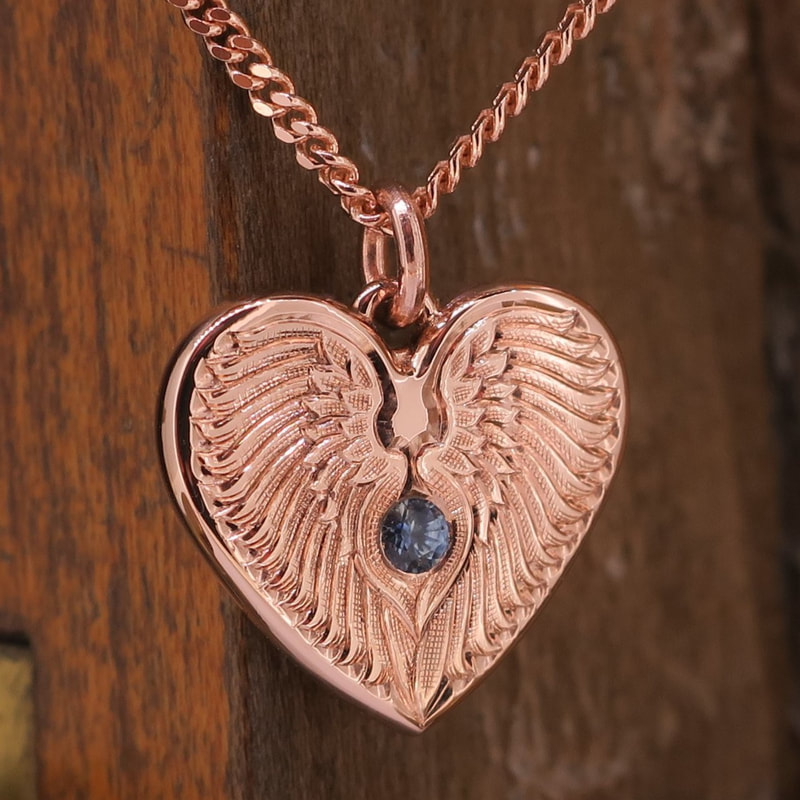 Rose gold heart pendant hand engraved with angle wings with a blue sapphire stone set in the centre